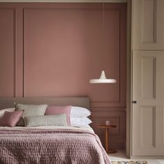 a bedroom with pink walls and bedding in the foreground is a doorway leading to another room