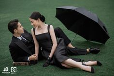 a man and woman sitting on the grass with an umbrella