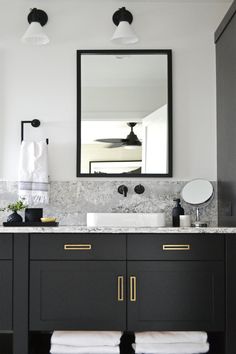 a bathroom with black cabinets and marble counter tops, white towels on the floor and a large mirror over the sink