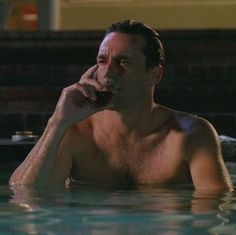 a man in the water drinking from a bottle and holding a cell phone to his ear