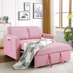 a pink couch with a blanket on it in front of a potted plant and window