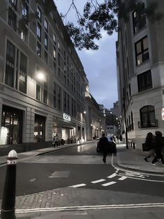 people walking down the street at night in an urban area with tall buildings on both sides