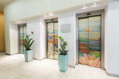 three tall planters with plants in them are next to glass doors that have paintings on them