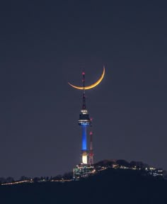 the moon is shining brightly in the night sky over a tall tower with a clock on it's side