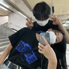 a woman wearing a face mask while looking at her cell phone with another person in the background