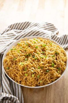 a white bowl filled with noodles on top of a wooden table next to a striped napkin