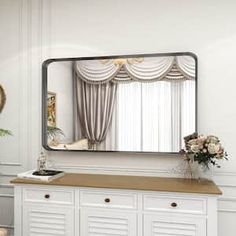 there is a large mirror on the wall above a dresser with drawers and vases