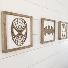 three wooden frames are hanging on the wall with various pictures in them, one has a spiderman mask and two have batman masks