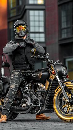 a man sitting on top of a motorcycle in front of a tall building wearing a helmet