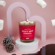 a candle that is sitting next to some marshmallows on a pink surface