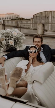 a man and woman sitting on top of a white car with flowers in the back