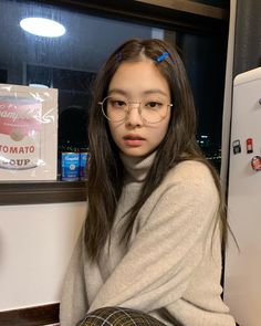 a young woman wearing glasses sitting in front of a refrigerator