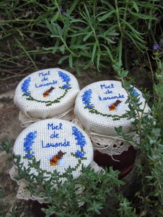 four embroidered coasters sitting on top of some grass and plants in front of bushes