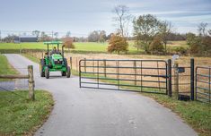 a tractor driving down a road next to a fence and grass covered field in the background