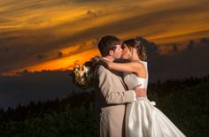 a bride and groom kissing in front of the sunset