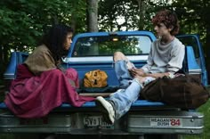 two people sitting on the back of a pick up truck with clothes in the bed