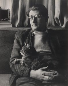 a man holding a cat in his arms while sitting on a couch next to a window