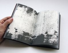 a hand holding an open book with black and white paint splattered on it