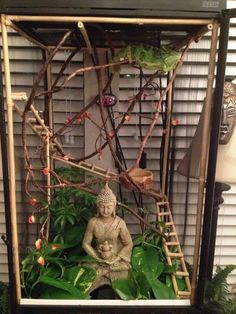 a small buddha statue sitting on top of a lush green plant covered ground in front of a window