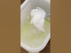 a white bucket filled with green liquid on top of a wooden floor next to a wall