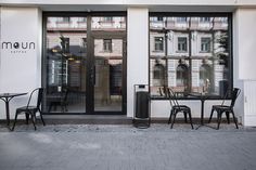 the outside of a restaurant with black tables and chairs in front of glass doored windows