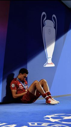 a man sitting on the ground in front of a wall with a trophy behind him