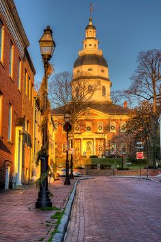 an old brick building with a clock tower in the background at sunset or dawn on a cobblestone street