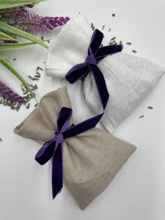 two small bags with purple ribbon tied to them sitting next to some lavender flowers on a white surface