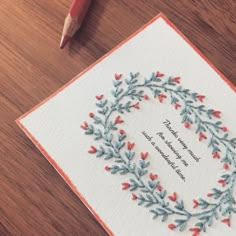 a handmade card with an embroidered wreath on it and a pencil next to it