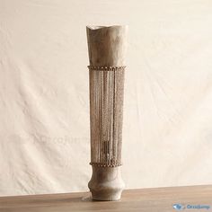 a tall wooden vase sitting on top of a table next to a white wall in the background