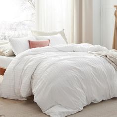 a bed with white comforter and pillows in a bedroom next to a window,