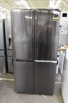 two stainless steel refrigerators in a warehouse with lots of other metal appliances behind them