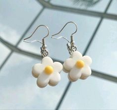 two white flowers with yellow centers are hanging from silver earwires on a glass surface