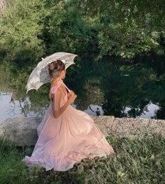 a woman in a pink dress is holding an umbrella by the water's edge