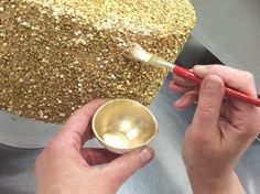 a person is painting a cake with gold flecks and a red handled spatula