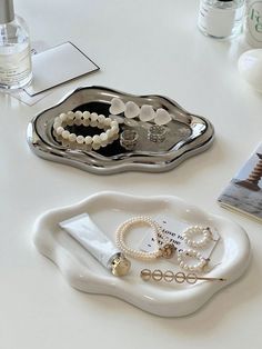 two white trays with pearls and jewelry on them