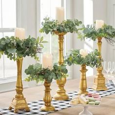 gold candlesticks with greenery in them on a checkered table cloth and place settings