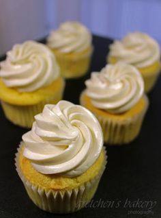 four cupcakes with white frosting sitting on a black table top next to each other