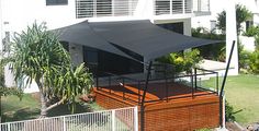 an outdoor patio area with wooden decking and black awnings on the side of a white building