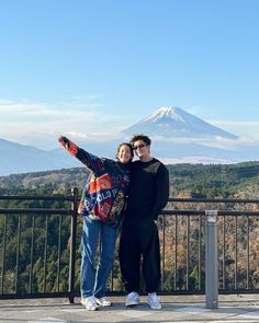 two people taking a selfie at the top of a hill with a mountain in the background