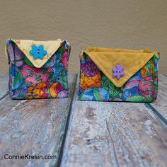 two purses sitting on top of a wooden table next to each other, one with a flower