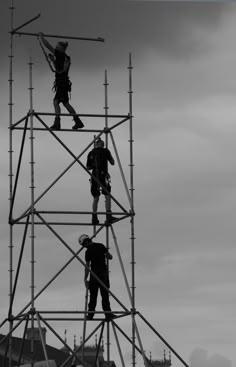 two men on scaffolding working on the top of a building in black and white