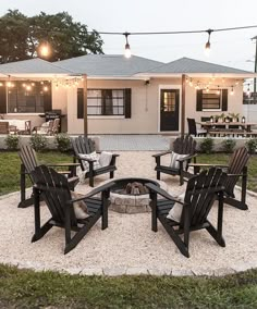 a fire pit surrounded by lawn chairs in front of a white house with string lights