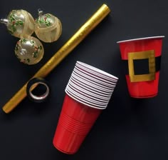 red cups with gold rims and decorations on black tablecloth next to christmas tree ornament