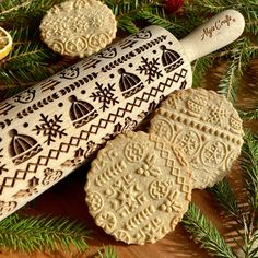 two cookies are next to a rolling pin on a wooden table with pine branches and decorations