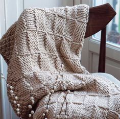 a knitted blanket sitting on top of a wooden chair next to a large window