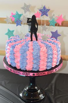 a cake with pink, blue and purple icing on it that has a person standing on top