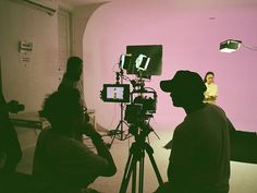 a group of people standing in front of a camera on a tripod with a pink wall behind them