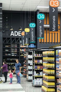 people shopping in a grocery store with signs hanging from the ceiling and shelves full of food