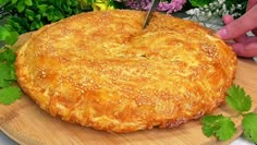 a person cutting into a large pie on top of a wooden board with flowers in the background